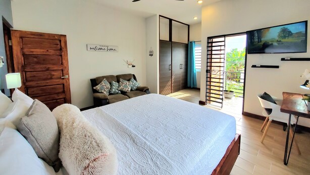 A bedroom with a bed, a desk, a ceiling fan, a wardrobe, and a sliding door to a balcony.