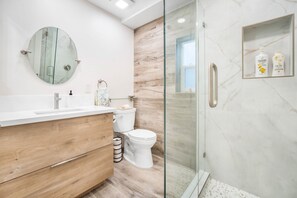 Un baño moderno con tocador de madera, cabina de ducha con vidrio y pared de mármol.