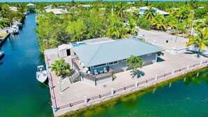 A waterfront property with a dock, a building with a flat roof, and surrounding greenery. - FISHERMANS DREAM HOUSE (Big Pine Key)