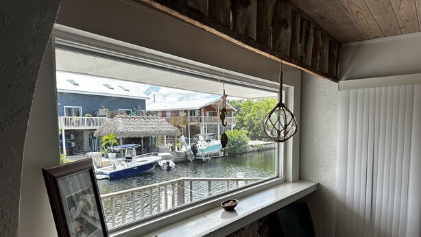 A room with a window overlooking a canal, a wooden ceiling, a framed picture on the window sill, and a small stool. - FISHERMANS DREAM HOUSE (Big Pine Key)