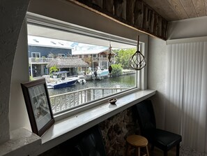 Une pièce avec une fenêtre donnant sur un canal, un plafond en bois, un tableau encadré posé sur le rebord de la fenêtre et un petit tabouret.