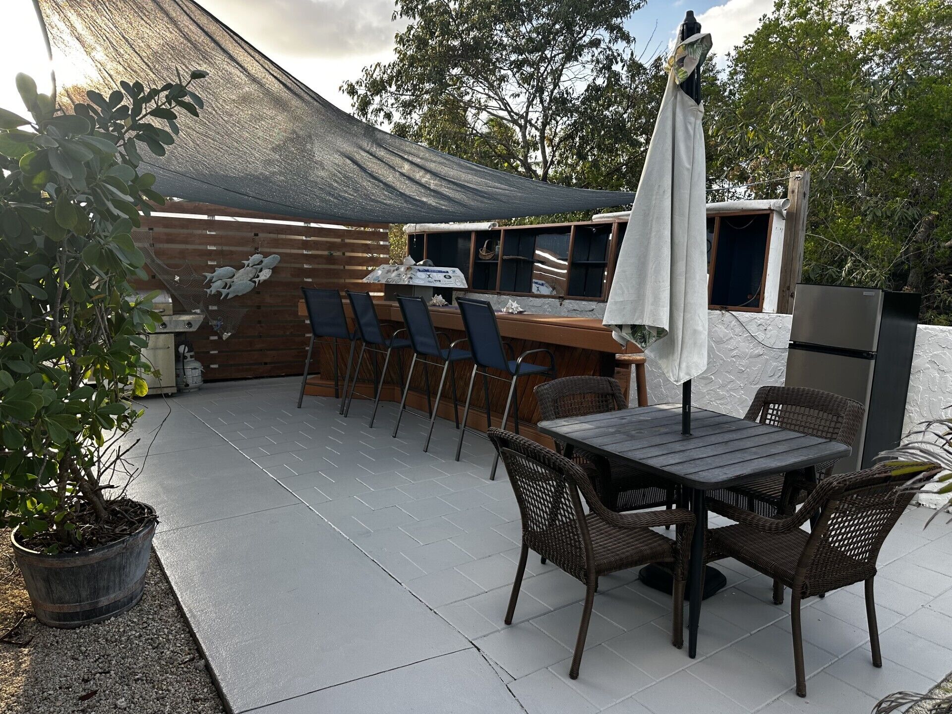 Une terrasse extérieure avec une table et des chaises en bois, un barbecue et un réfrigérateur.