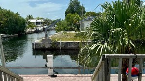 A wooden dock leading to a calm water body with a small pier, surrounded by greenery and a clear sky. - FISHERMANS DREAM HOUSE (Big Pine Key)