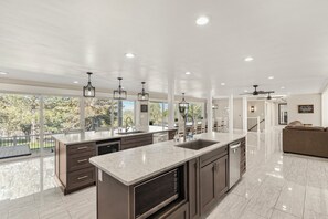 A modern kitchen with a large island, dark cabinetry, and a view of the outdoors. - Large luxury home with a pool, playground & a view! (Pocatello)