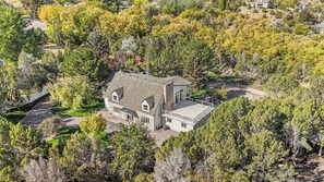 A large, two-story house surrounded by dense trees, with a visible driveway and a small deck area. - Large luxury home with a pool, playground & a view! (Pocatello)