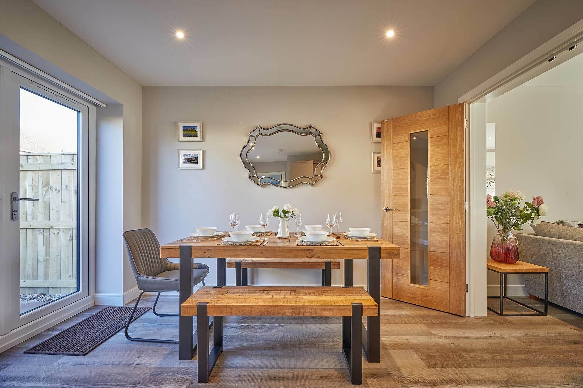 Een eetruimte met een houten tafel voor vier personen, een bank en een grote spiegel aan de muur.