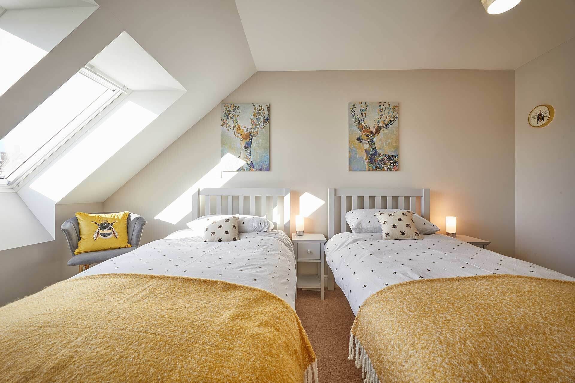 A bedroom with two beds, a skylight, and two paintings on the wall.