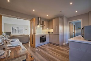 A modern kitchen with wooden flooring, built-in appliances, and a dining area with a wooden table set for four. - Host Stay Sunflower Cottage (Seahouses)