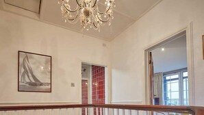 Un intérieur spacieux avec un plafond haut, un lustre, un escalier doté d’une rampe en bois et un mur recouvert de carreaux rouges.