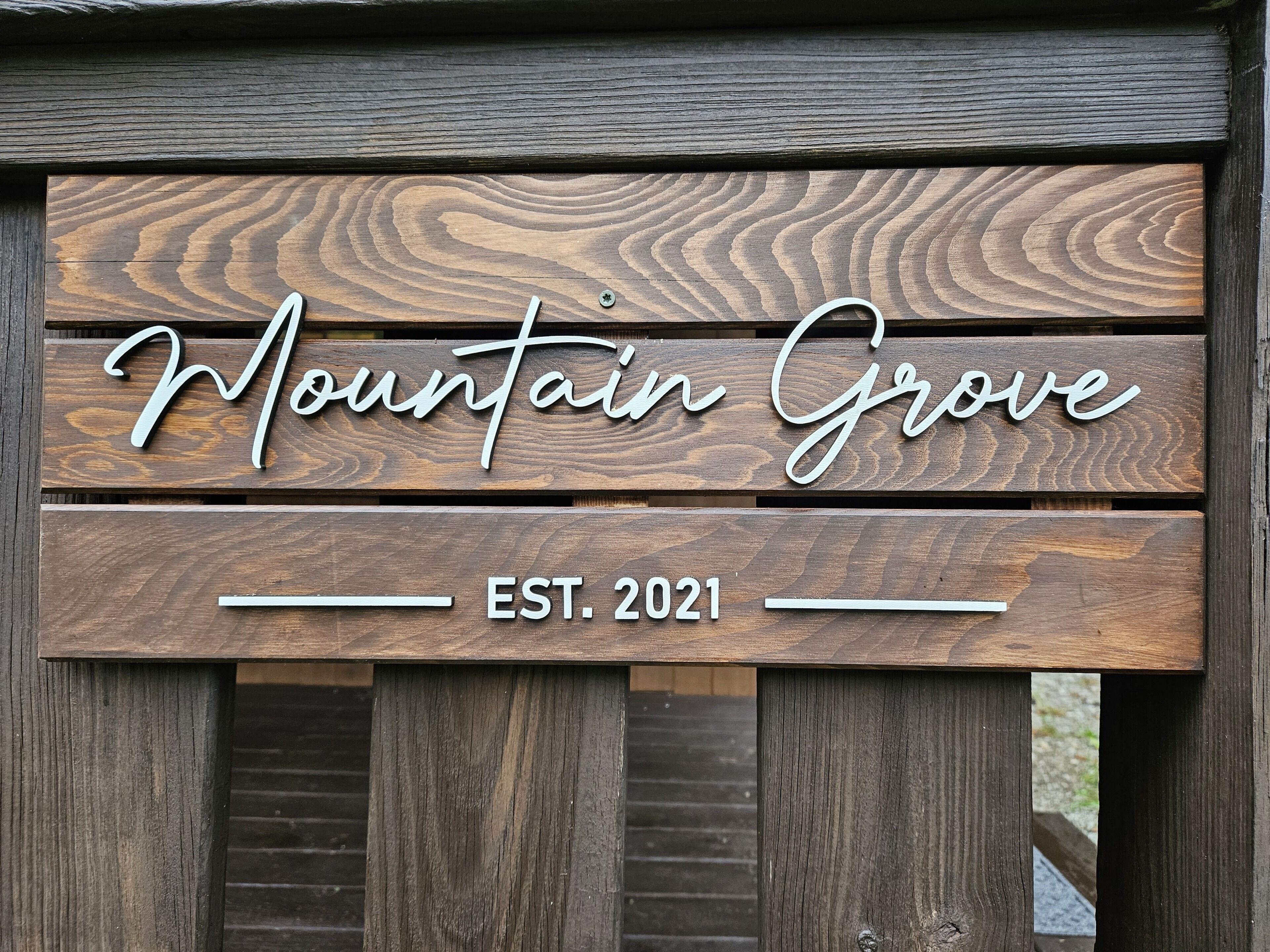 En träskylt med texten ”Mountain Grove, grundat 2021” på ett trästaket.