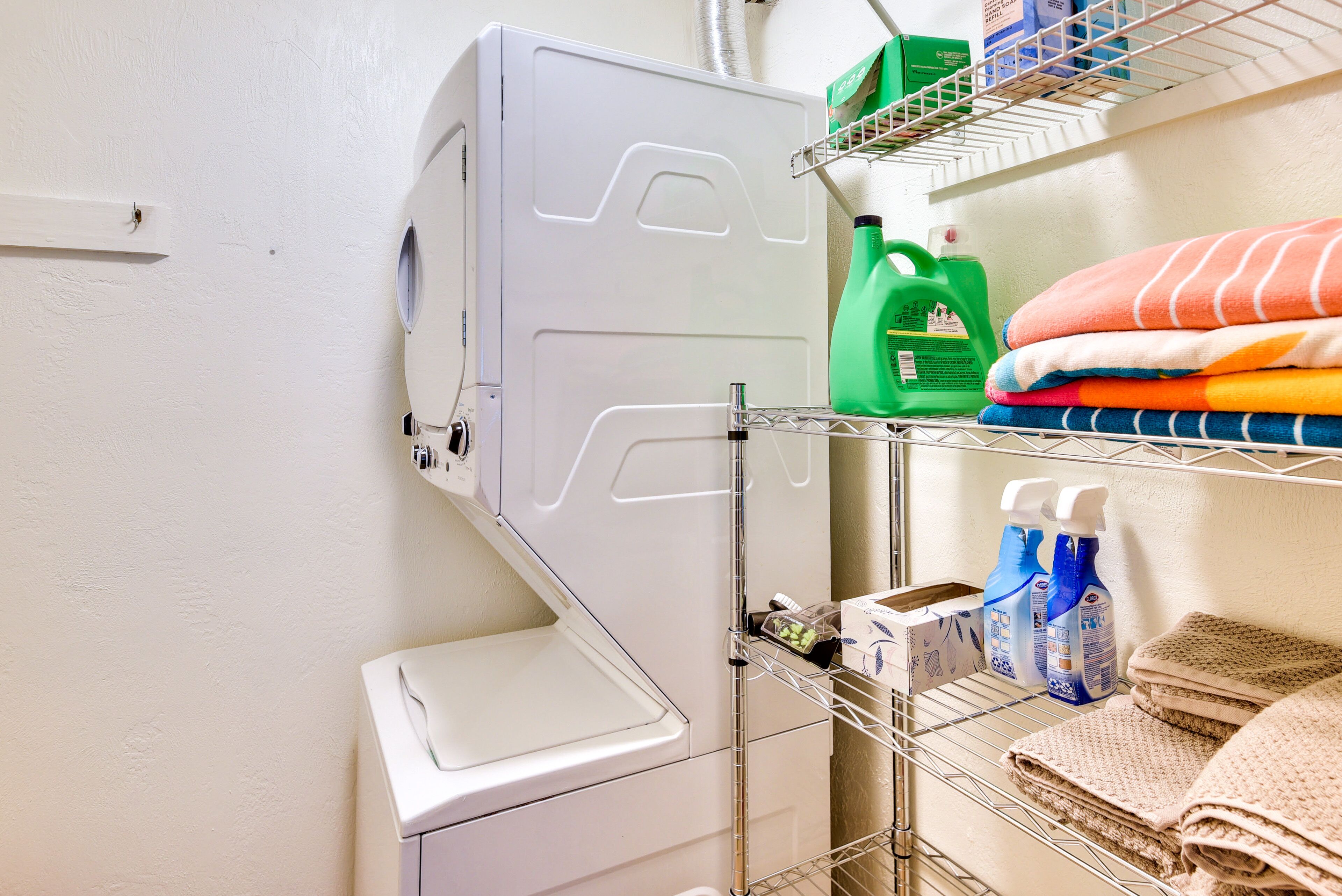 A laundry area with a washing machine, shelves with folded towels, and cleaning supplies.