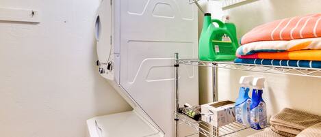 A laundry area with a washing machine, shelves with folded towels, and cleaning supplies.