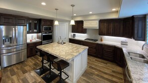 Una cocina moderna con electrodomésticos de acero inoxidable, armarios de madera oscura y una isla de encimera de granito con taburetes de bar.