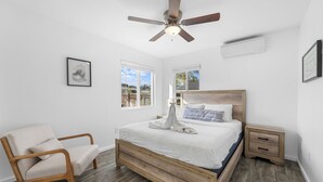 A bedroom with a wooden bed, a chair, a ceiling fan, and two windows. - Charming El Cajon Retreat  (El Cajon)
