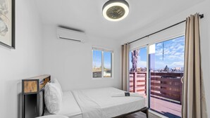 A modern bedroom with a bed, a small table, a window, and a view of the city. - Charming El Cajon Retreat  (El Cajon)