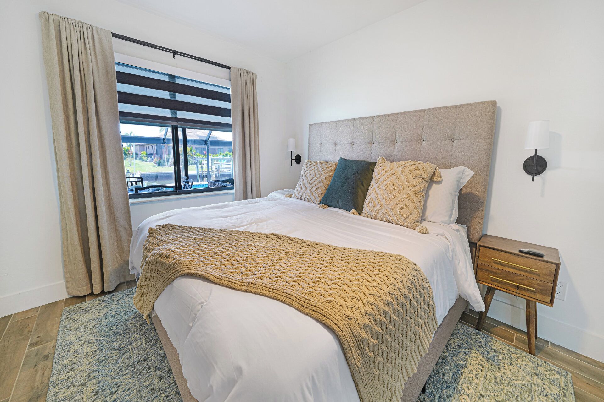 Une chambre à coucher avec un grand lit, une tête de lit, une table de chevet, une lampe et une fenêtre avec des rideaux.