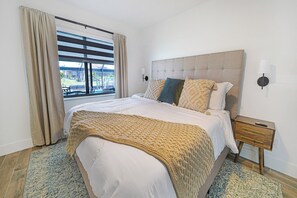 A bedroom with a large bed, a headboard, a nightstand, a lamp, and a window with curtains. - VRCC Villa Cape Escape (Cape Coral)