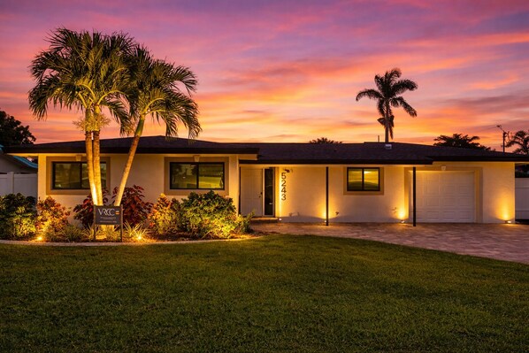 A two-story house with a garage, a well-maintained lawn, and a signboard. - VRCC Villa Cape Escape (Cape Coral)
