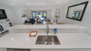Una cocina moderna con una isla grande, pileta de acero inoxidable y muebles color blanco.