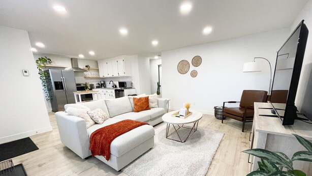 Uma sala de estar moderna com um sofá branco, uma mesa de centro e um rack para TV.