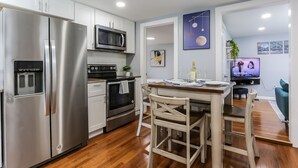 A modern kitchen with stainless steel appliances, a dining area with wooden chairs, and a TV displaying 'NEW AMSTERDAM'. - 2 BEDROOM APARTMENT IN BRISTOL NEAR PLAINVILLE  (Bristol)