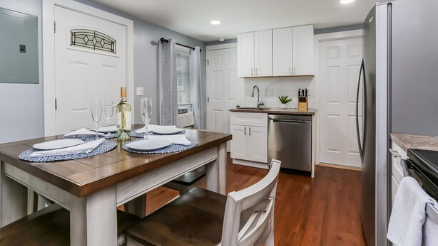 A modern kitchen with white cabinets, a stainless steel refrigerator, and a dining area with a wooden table set for two. - 2 BEDROOM APARTMENT IN BRISTOL NEAR PLAINVILLE  (Bristol)