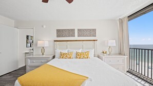 Quarto de hotel com uma cama grande, duas mesas de cabeceira com luminárias, uma cabeceira e vista para o oceano através de uma varanda.