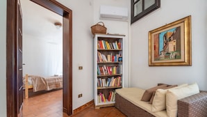 Une pièce comprenant un lit, une bibliothèque, un canapé en osier et un tableau accroché au mur.