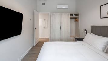 Un dormitorio con cama, armario, mesita de noche y televisor de pared.