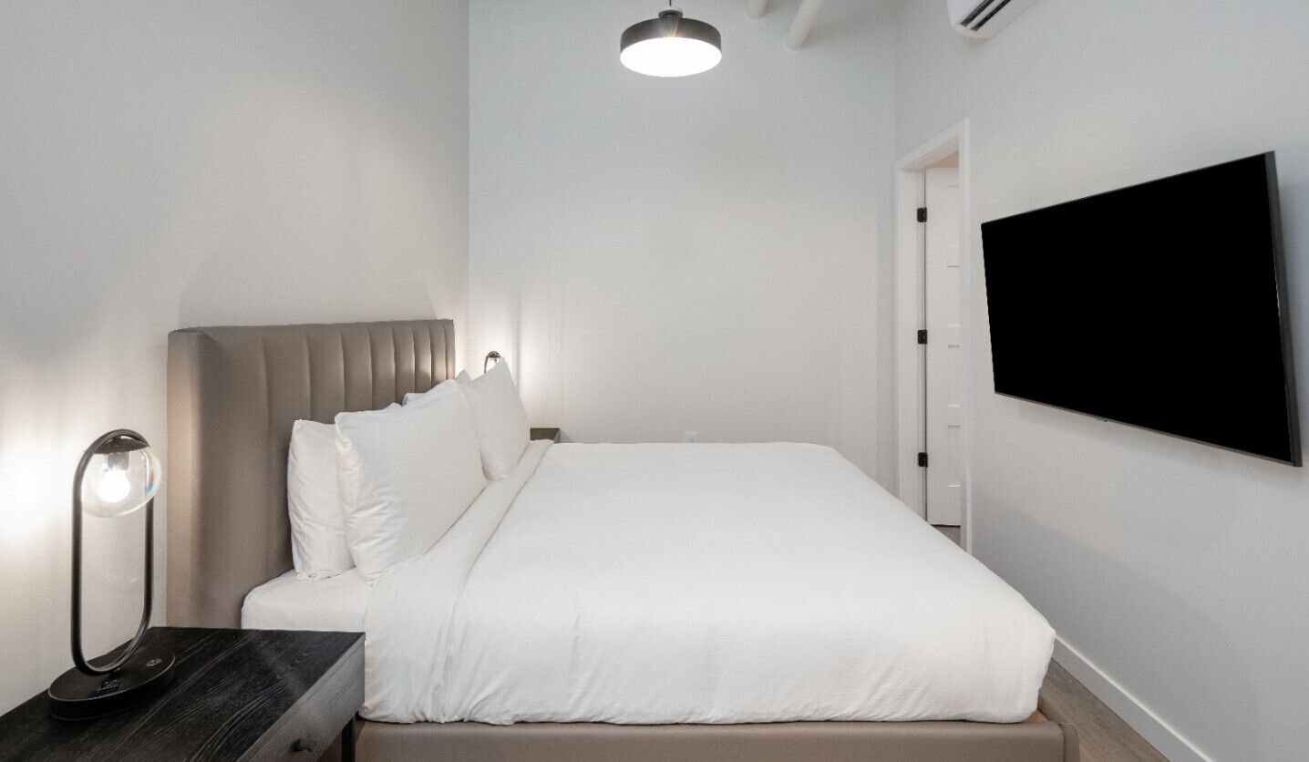 A modern bedroom with a bed, bedside table, lamp, and a TV mounted on the wall.