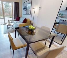 Una sala de estar moderna con una mesa de vidrio, sillas color beige, un sofá con cojines rojos y una mesa de centro con una planta.