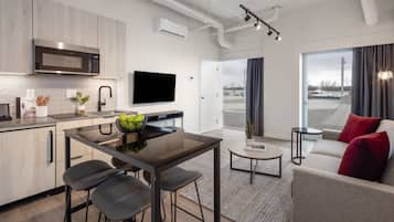 Una cocina moderna con microondas, mesa de comedor y taburetes de bar. Hay un televisor de pantalla plana montado en la pared y un ventanal con vistas al exterior.
