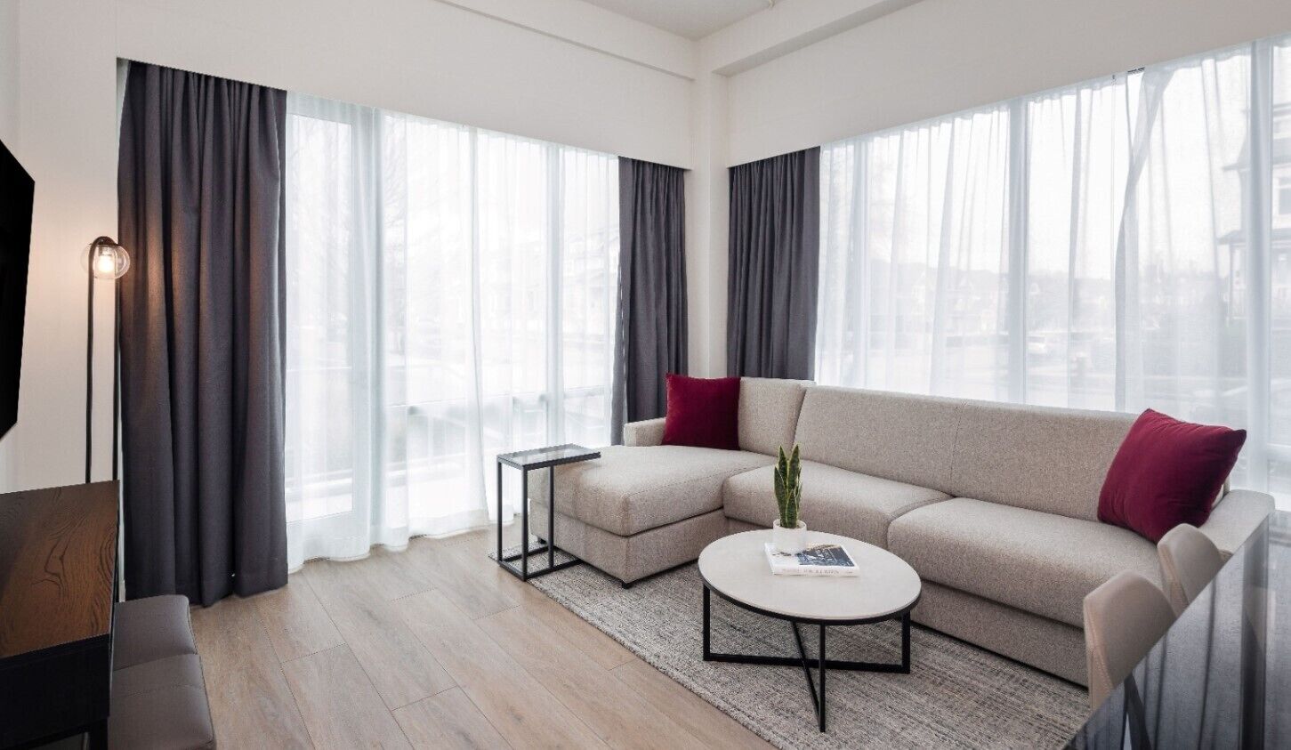 Un soggiorno moderno con un divano angolare beige, un tavolino rotondo, un comodino e una lampada da terra.