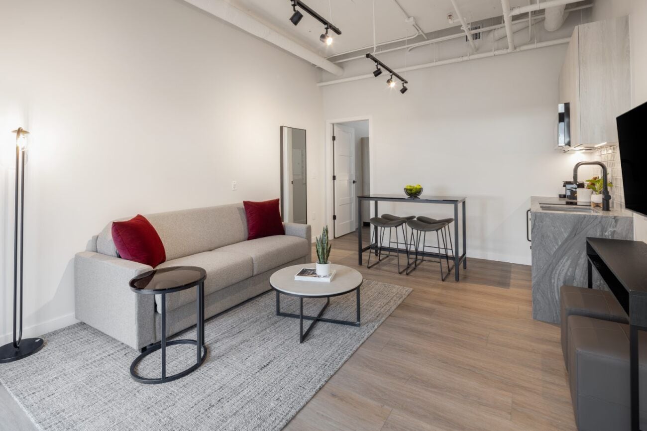 A modern living room with a sofa, coffee table, and a small dining area.