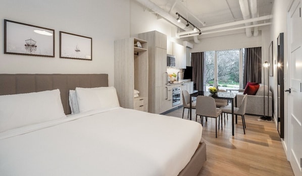 Una habitación de hotel moderna con una cama grande, un área de comedor con mesa y sillas, y vistas al exterior.