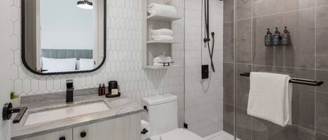 A modern bathroom with a toilet, sink, and shower. There are towels and toiletries on the shelves.