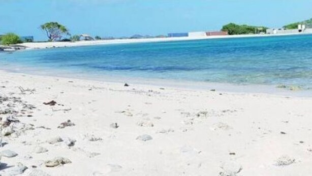 Une plage avec une eau d’un bleu limpide, du sable blanc et un promontoire rocheux qui se dessine à l’horizon.