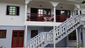 Un immeuble de deux étages avec un balcon à l’étage supérieur, un escalier et une porte rouge.
