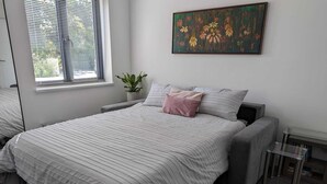 Une chambre à coucher moderne avec un grand lit, une petite table de chevet, une plante en pot et un tableau accroché au mur.