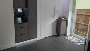 Une cuisine moderne avec des meubles de couleur bois foncé, une porte blanche et un petit plan de travail sur lequel se trouve une bouilloire.