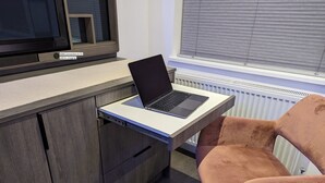 Un bureau moderne équipé d’un ordinateur portable, d’une chaise et d’un téléviseur doté de ports HDMI et USB pour le chargement.