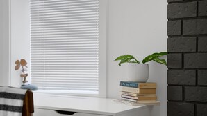 A white desk with a plant, a stack of books, and a window with blinds. - Modern 1 Bed Suite Close to Town & Westwood Lake (Nanaimo)