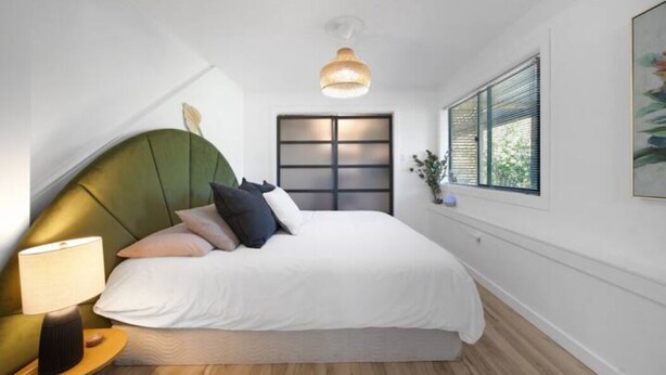 A modern bedroom with a green upholstered headboard, a white bedspread, and a bedside lamp. - Modern 1 Bed Suite Close to Town & Westwood Lake (Nanaimo)