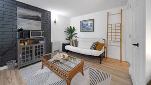 A modern living room with a grey brick wall, a white sofa, a glass coffee table, and a wooden floor. - Modern 1 Bed Suite Close to Town & Westwood Lake (Nanaimo)