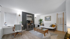 A modern living room with a white sofa, a glass coffee table, a wooden desk, and a fireplace. - Modern 1 Bed Suite Close to Town & Westwood Lake (Nanaimo)