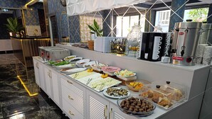 Montaje tipo bufé con diversos alimentos, una máquina de café y un jarrón decorativo.
