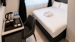 Habitación de hotel con cama, escritorio, hervidor de agua, botellas de agua, una silla y televisor.