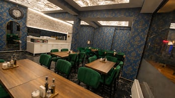 A restaurant with a modern ceiling design, green upholstered chairs, and a wooden dining table.