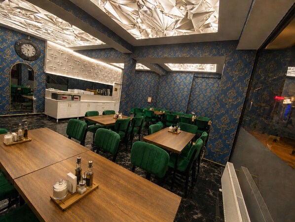 Un restaurante con un diseño moderno en el techo, sillas tapizadas de verde y una mesa de comedor de madera.