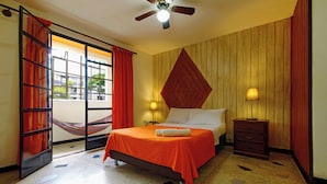 A hotel room with a bed, a nightstand, a lamp, a ceiling fan, a hammock, and a window with curtains. - Ding-Dong Hostel (Cali)